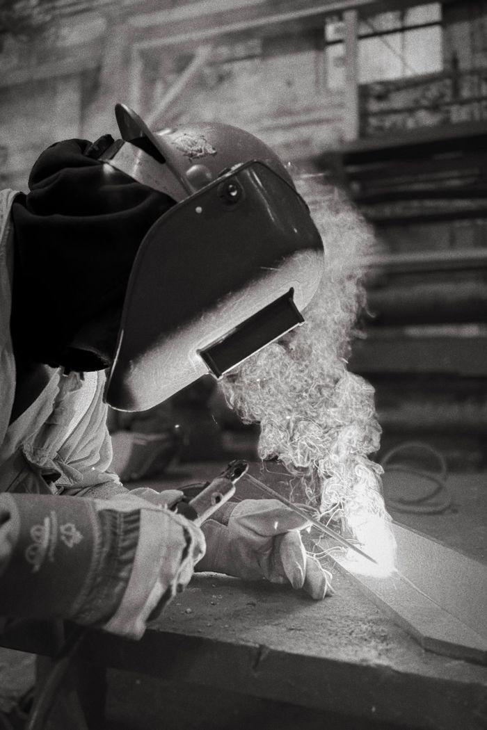 Black and white image of a welder creating sparks, wearing protective gear in an industrial setting.