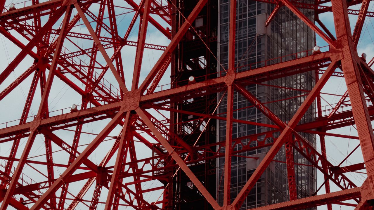 contact-img Detailed view of the red steel beams of a tower structure against the clear sky.