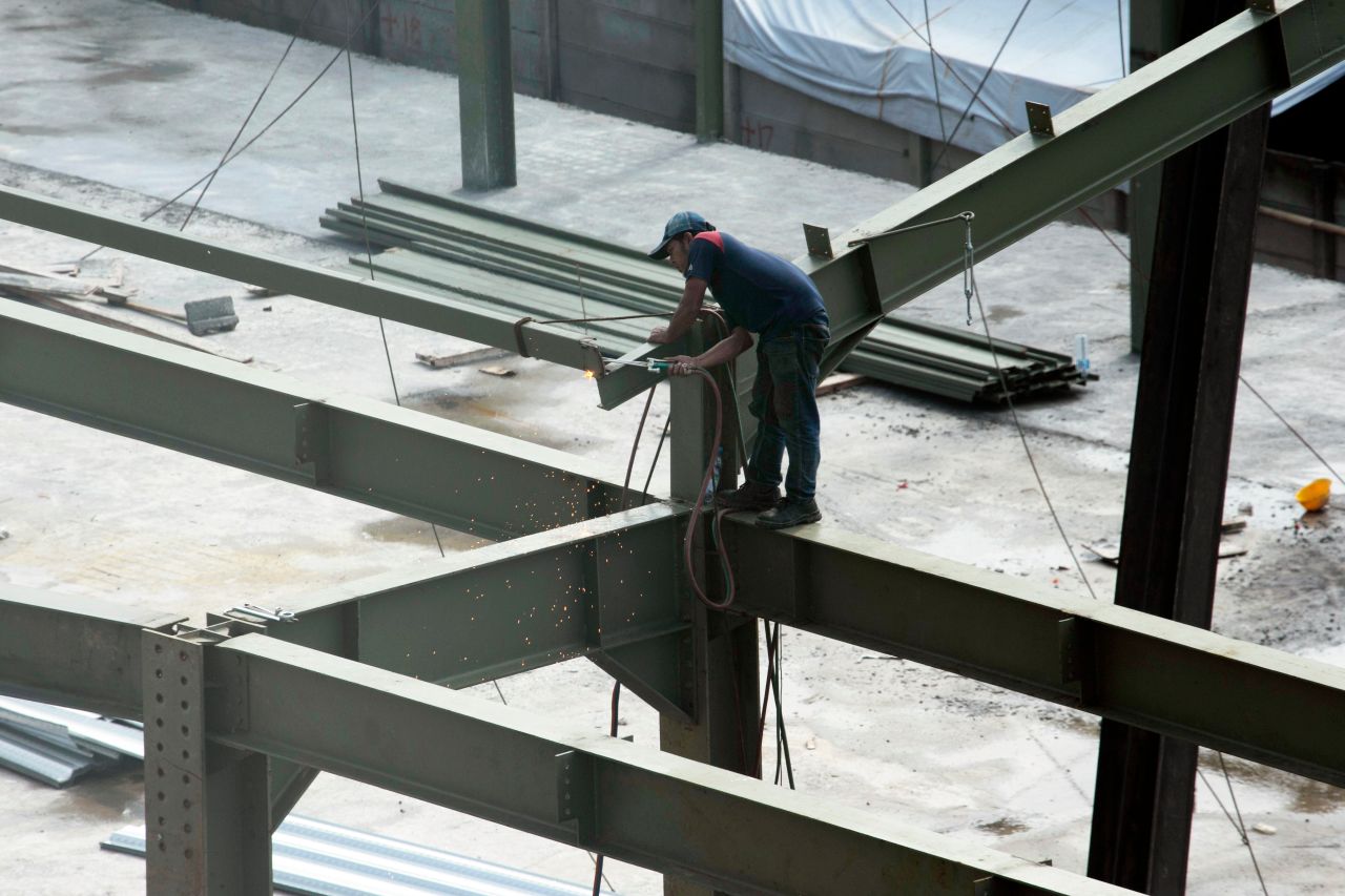 A construction worker welding steel beams on a high-rise construction site. Sparks fly as the worker welds.